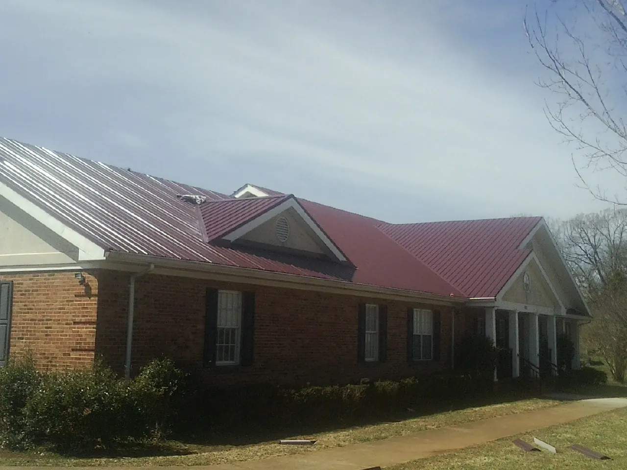 Red metal roof with gabled entries on a long brick building, from a Hail Damage Roof Repair job in Fannettsburg