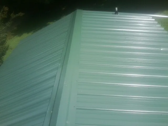 New green metal panels meeting at the ridge of a roof — Flat Roof Repair work by our crew in Fannettsburg
