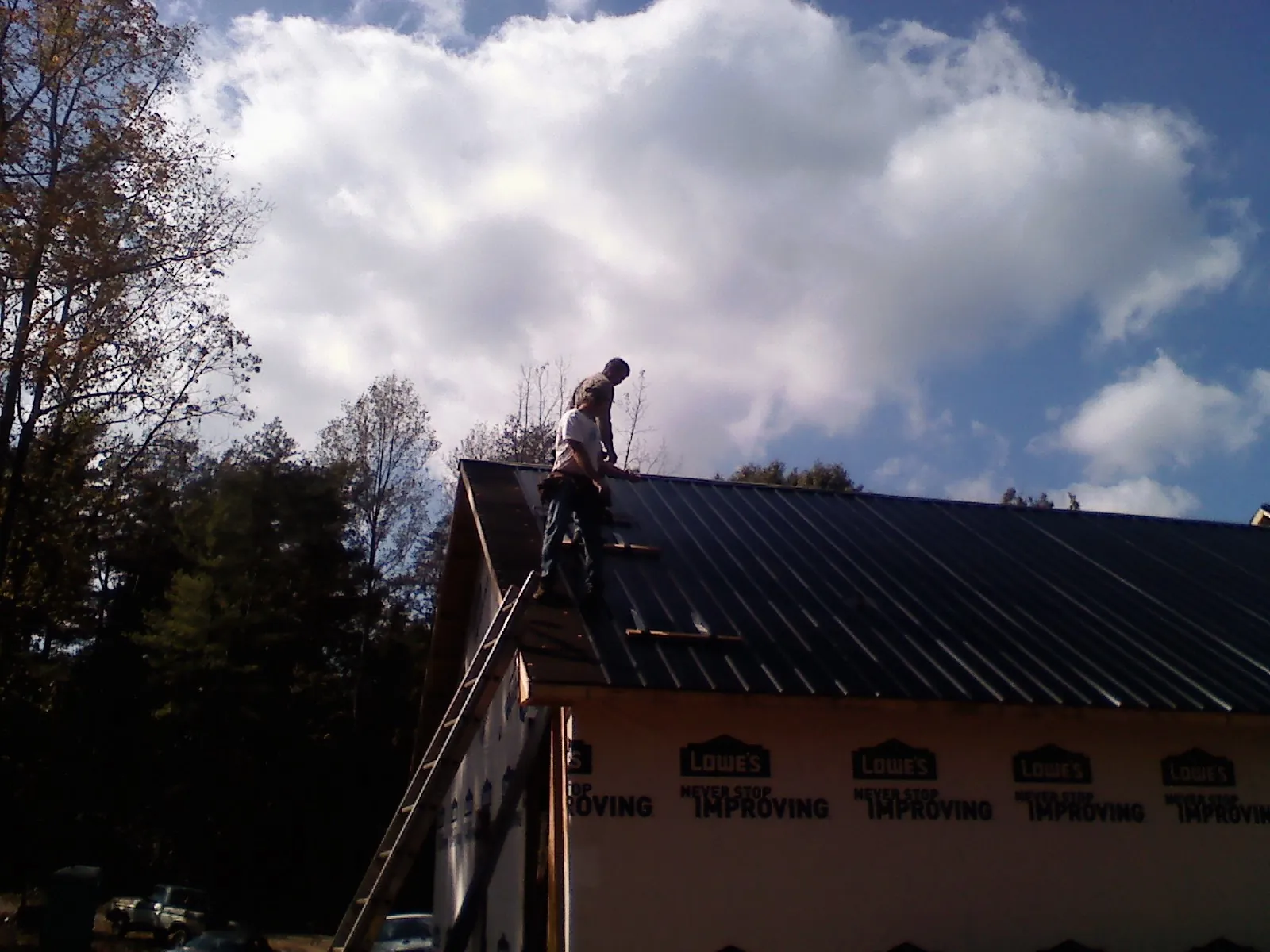 Roofer fastening dark metal panels high against a cloudy sky, from a Roof Inspection job in Fannettsburg