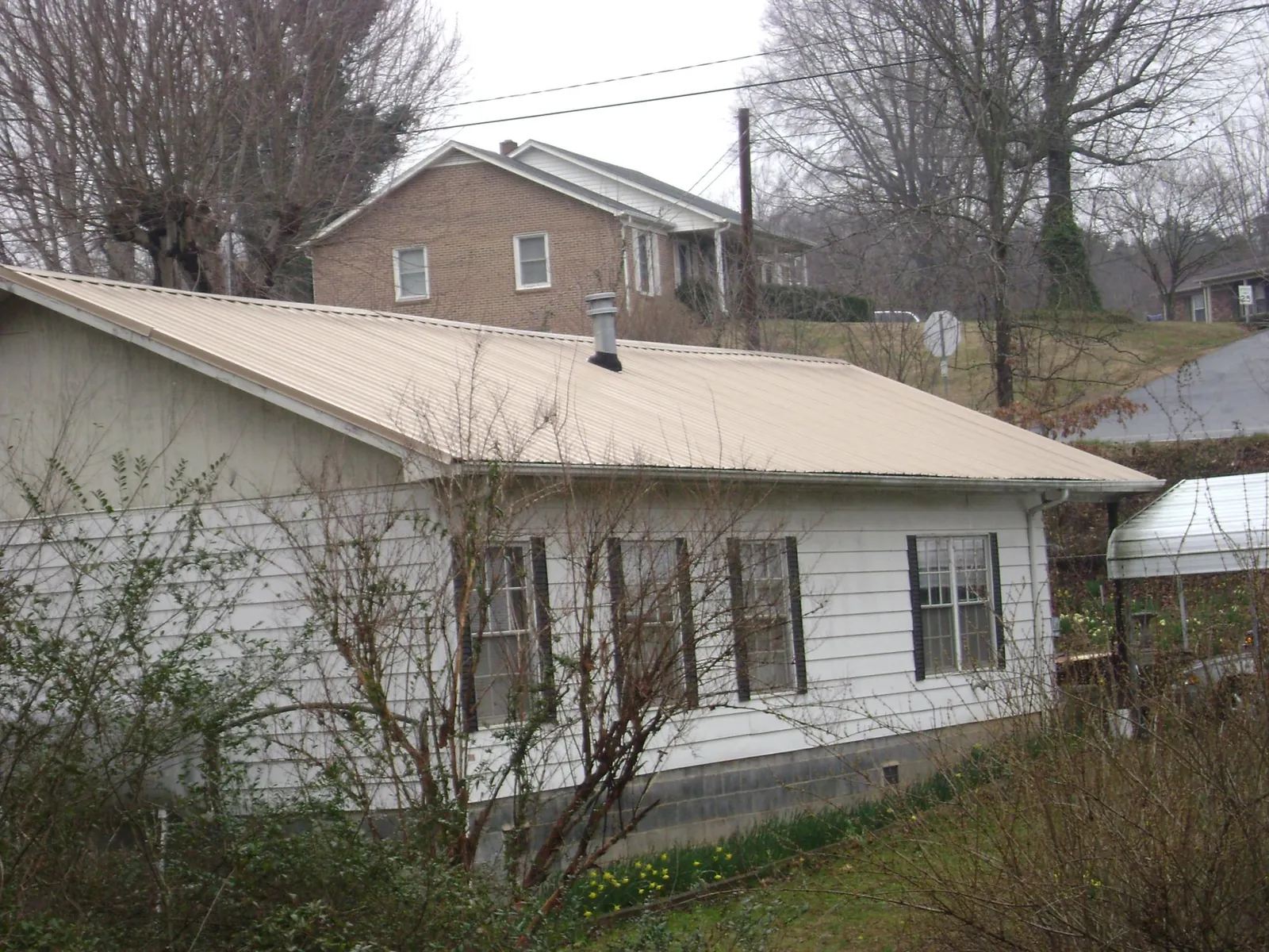 Tan metal roof on a white sided house set into a hillside — Commercial Roofing by Roofing Brothers in Fannettsburg